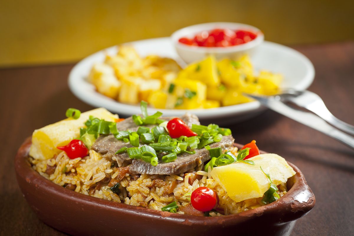 Baião de dois served in a clay bowl, with beef, cassava and biquinho peppers